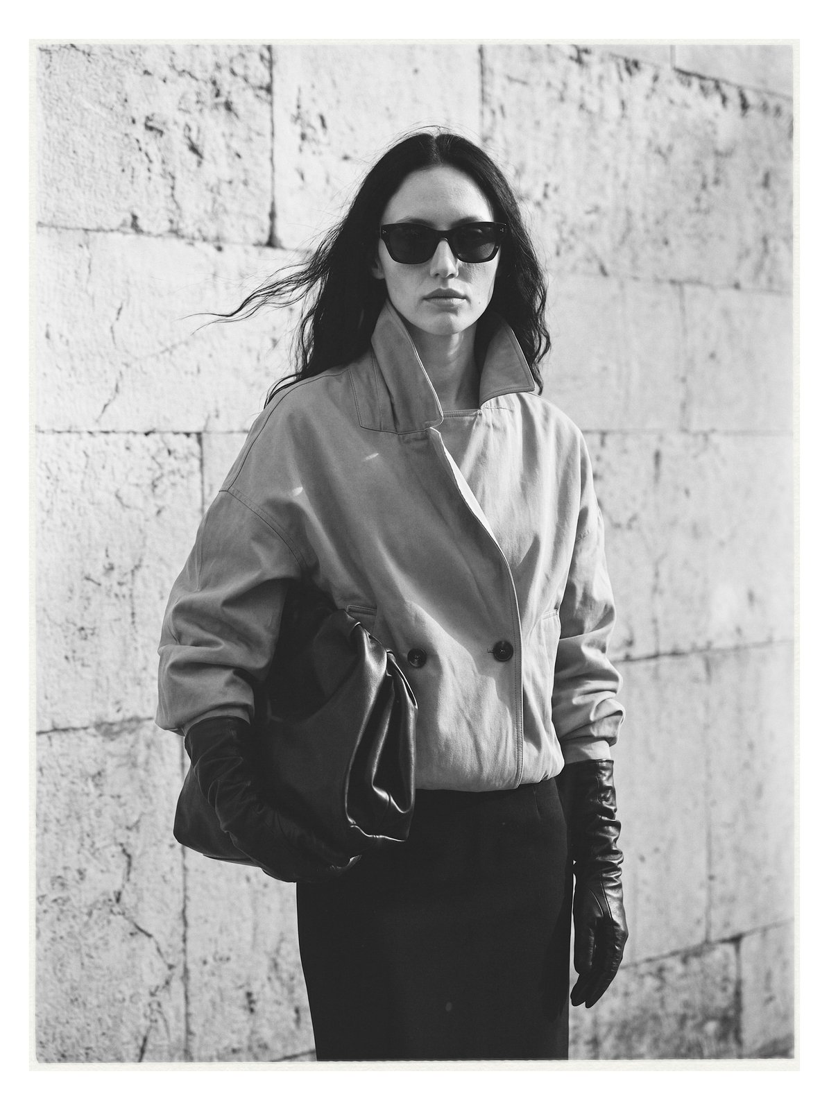 Street editorial: full-length figure in a grey coat against a stone wall